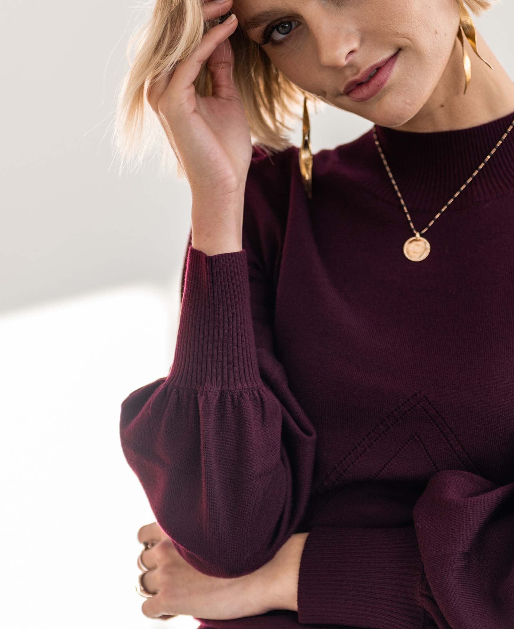 Woman wearing a PLEIN PUBLIQUE Bordeaux turtleneck sweater, touching her head.