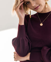 Woman wearing a PLEIN PUBLIQUE Bordeaux turtleneck sweater, touching her head.