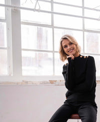 Merino wool sweater LA CLIQUE Black-gold by PLEIN PUBLIQUE shown near large windows in a minimalist room.
