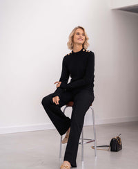 Black and gold merino wool sweater by PLEIN PUBLIQUE, LA CLIQUE style, shown on a seated model.