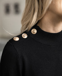 Close-up of the Merino wool sweater LA CLIQUE in black-gold by PLEIN PUBLIQUE, featuring gold shoulder buttons.