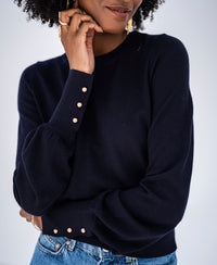 Woman wearing a PLEIN PUBLIQUE Merino wool sweater LA MARIS in dark blue-gold, smiling softly.