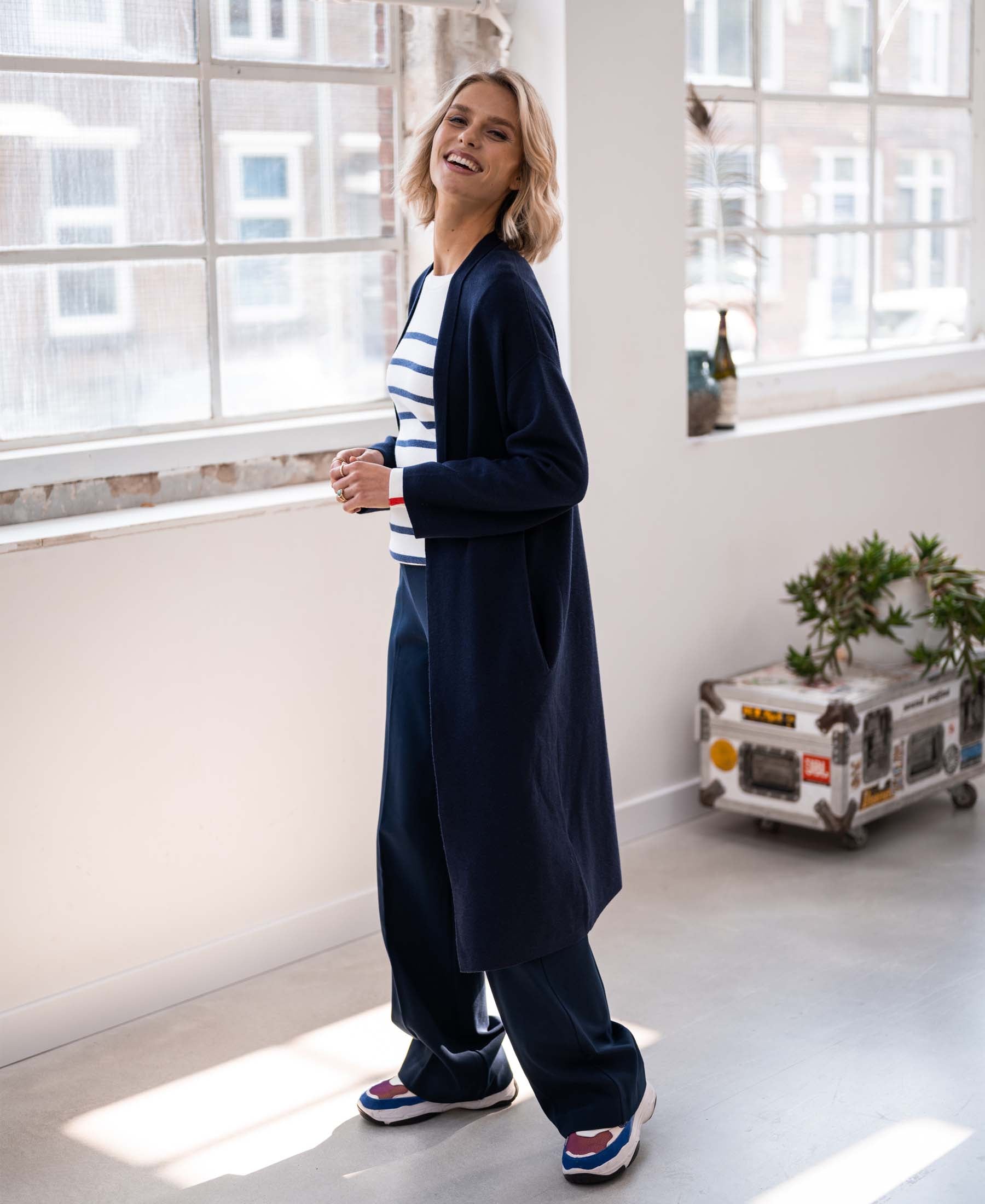 A blonde woman wears a navy Breton sweater in ivory and denim blue from PLEIN PUBLIQUE.