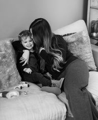 Woman wears anthracite knitted trousers as she sits on a couch.