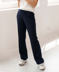 Model wears dark blue knitted trousers LE LOURDES by PLEIN PUBLIQUE indoors in sunlight.